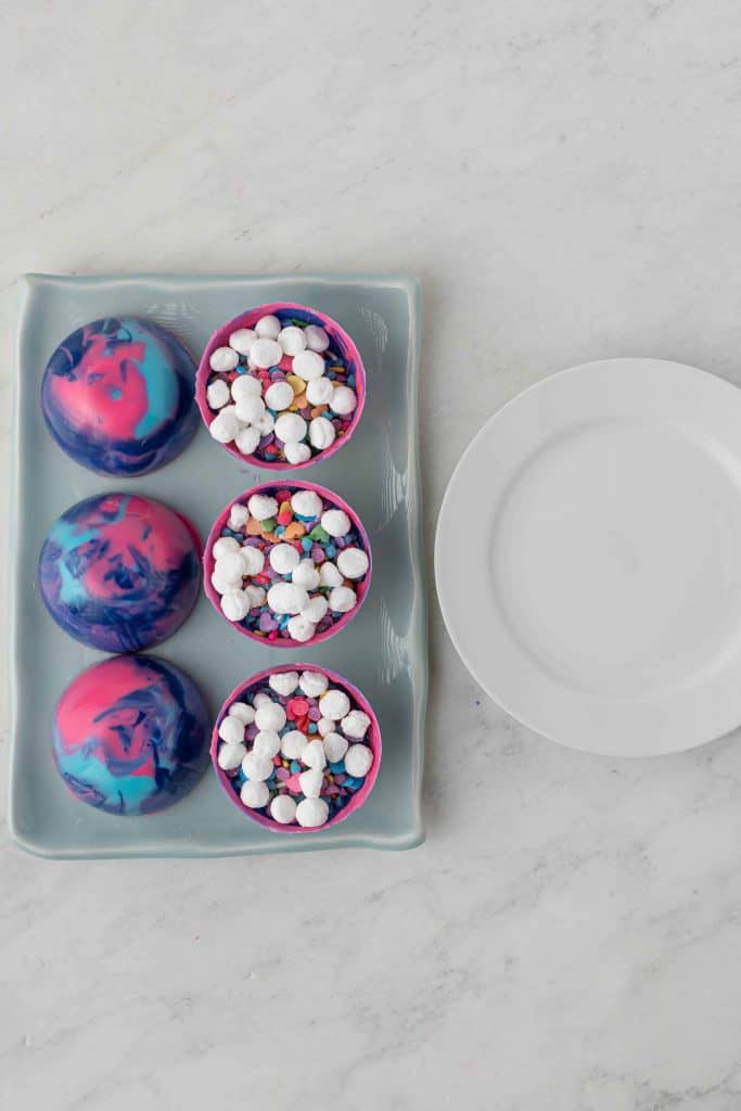 Galaxy hot cocoa bombs being prepared with mini marshmallows on top.