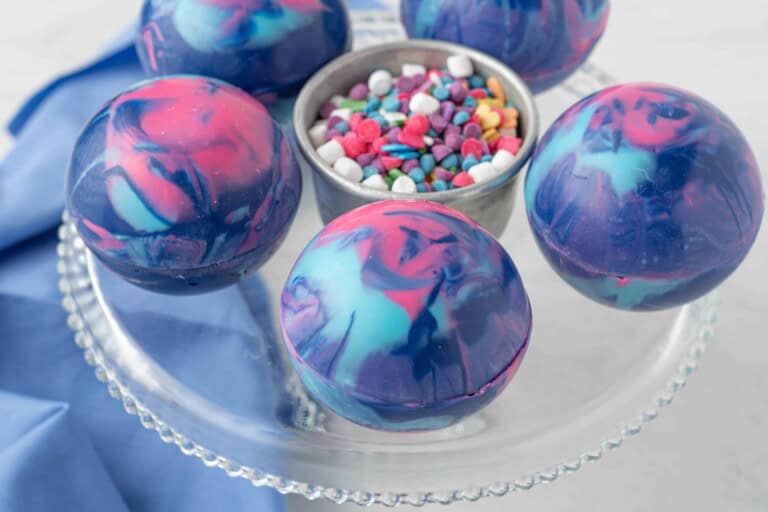 3/4 angle view of galaxy hot cocoa bombs on a glass cake stand.