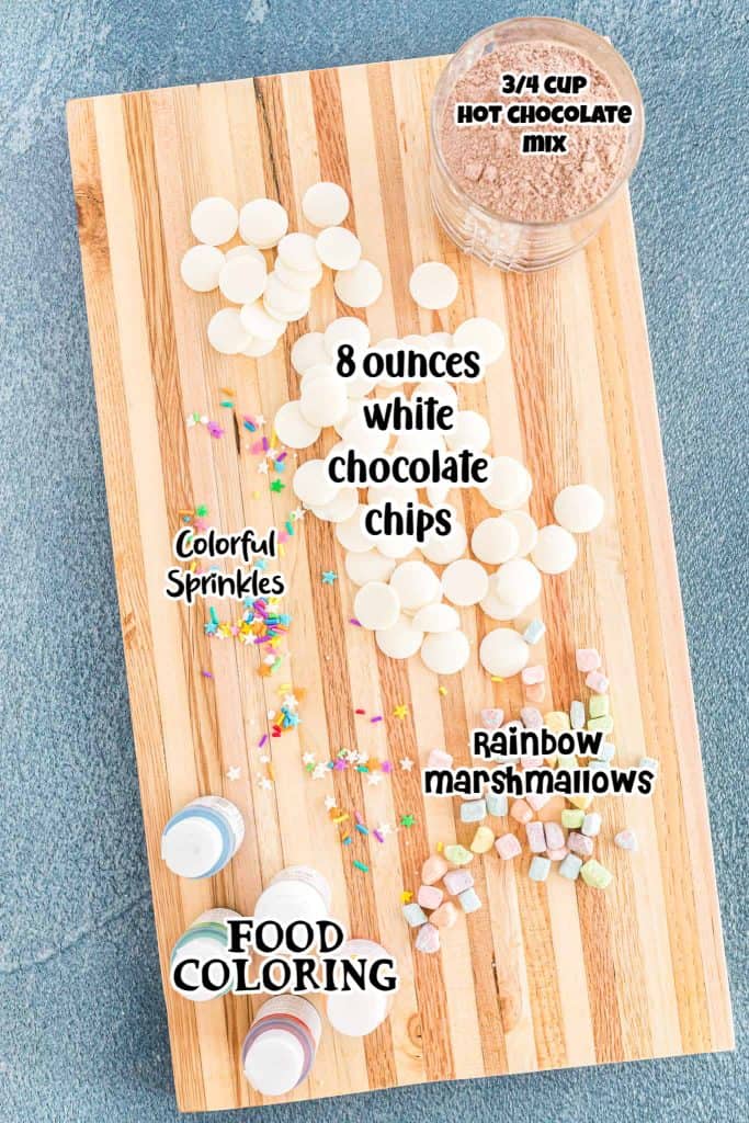 white chocolate, hot chocolate mix, food coloring, sprinkles and rainbow mini marshmallows on a wood cutting board.