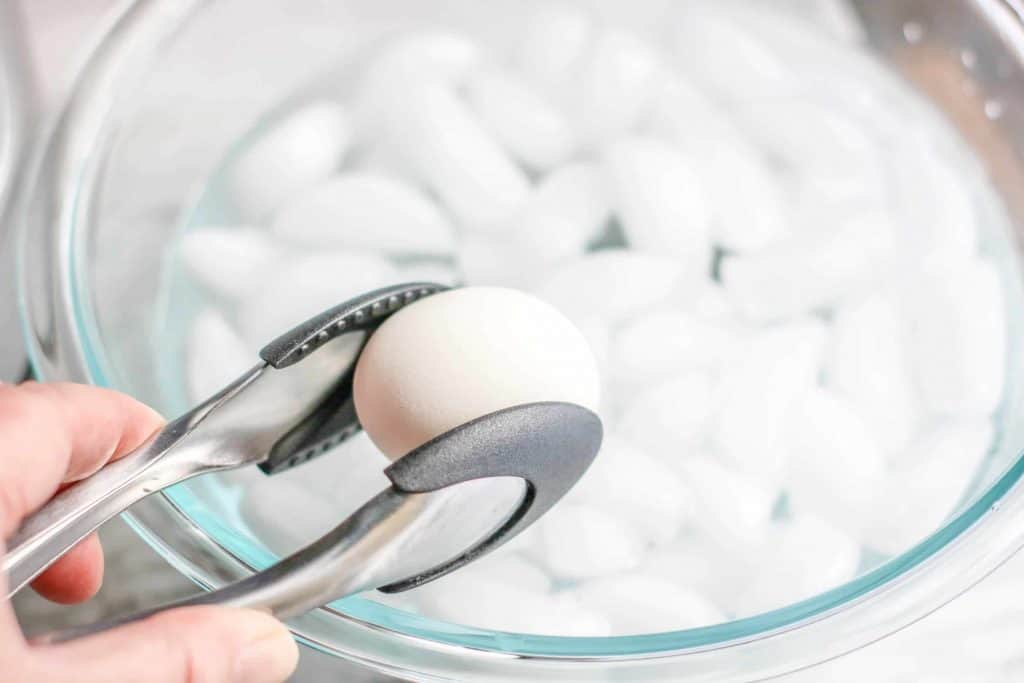 using tongs to place hard boiled egg in an ice water bath.
