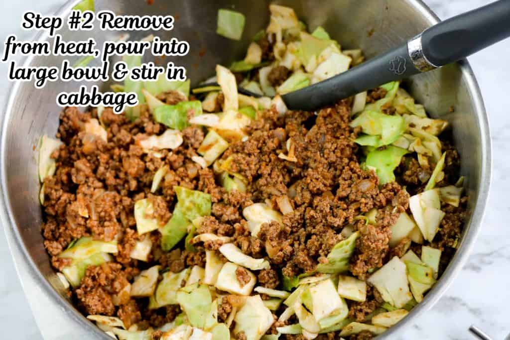 Cooked ground beef with fresh green cabbage being mixed in large stainless steel bowl.