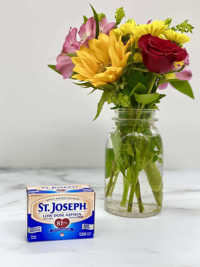 St. Joseph's aspirin on a marble countertop with a vase of spring flowers in the background.