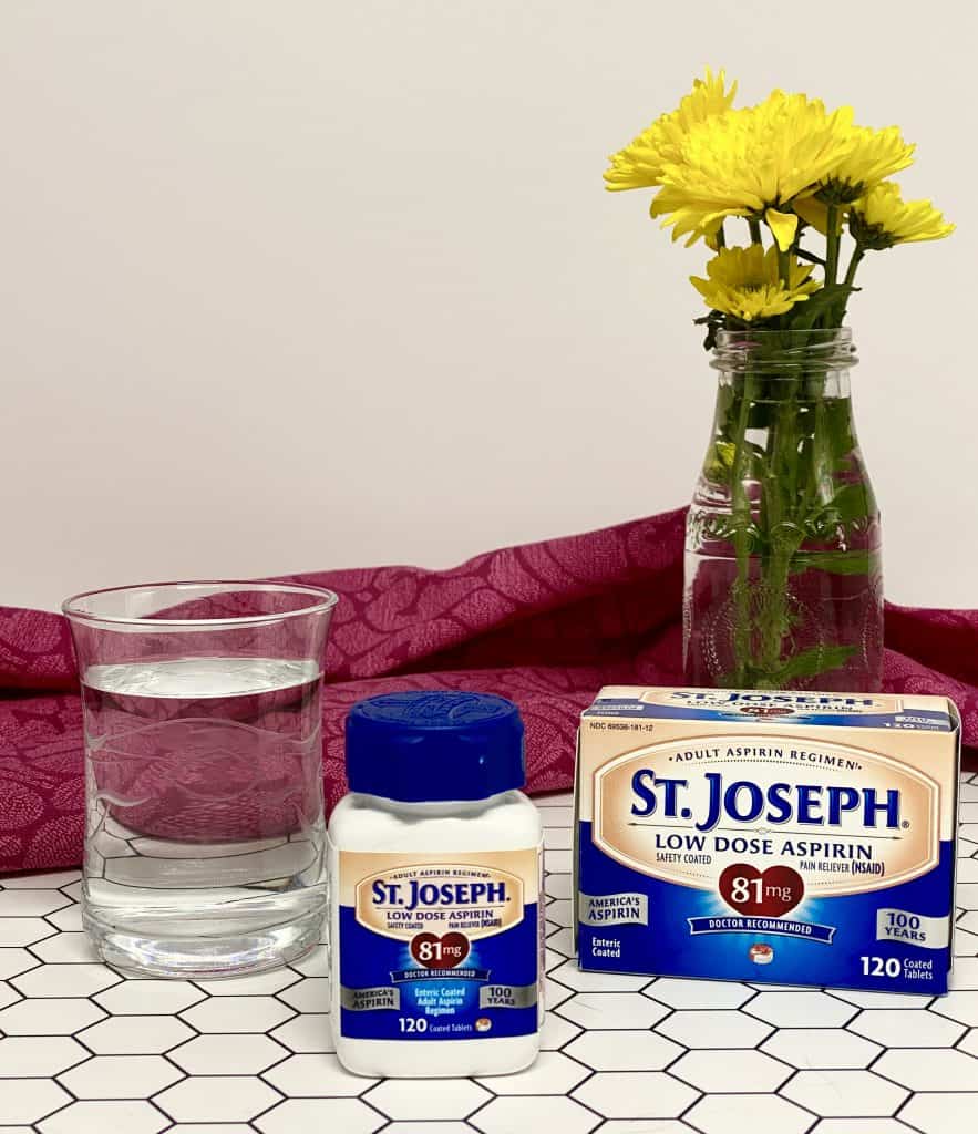 St. Joseph's Aspirin on a bathroom counter top with a glass of water and a vase of yellow flowers in the background.