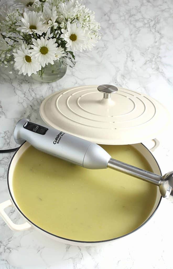 Asparagus soup in a beige pot with an immersion blender on top of it.