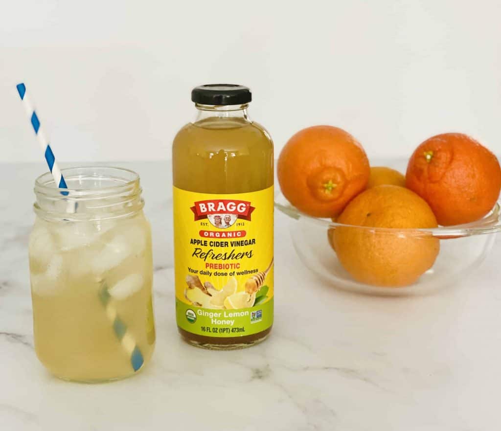 BRAGG Apple Cider Vinegar Refresher with bowl of oranges behind it.