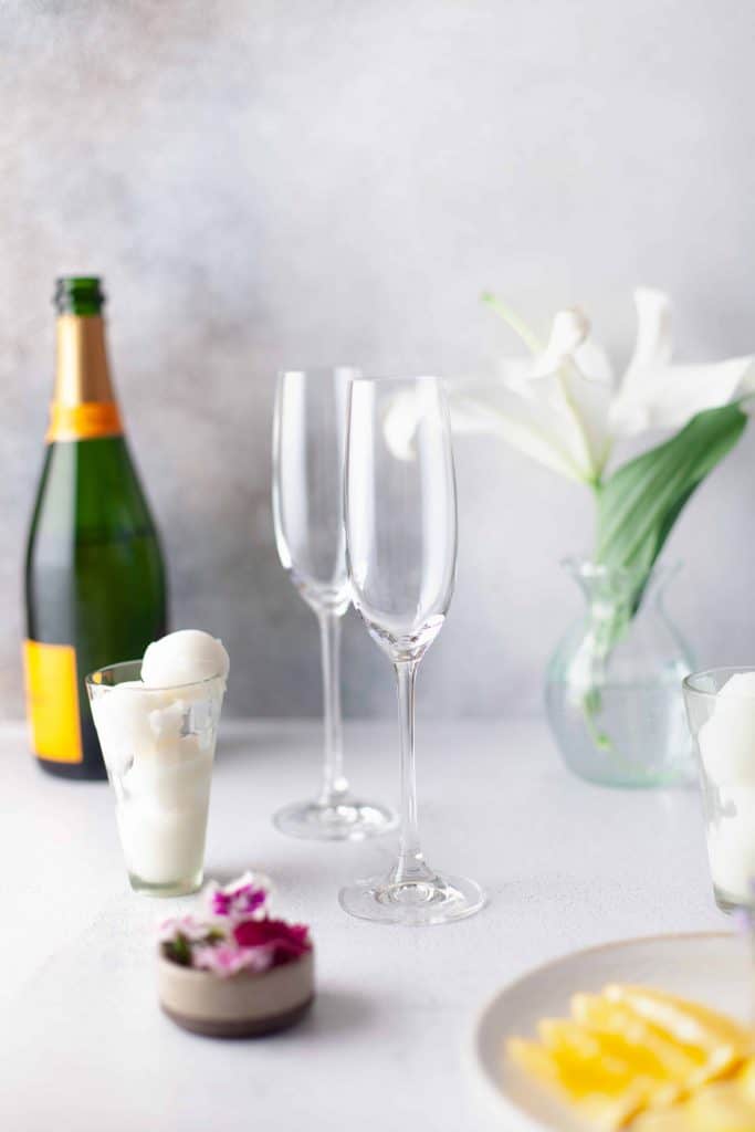 Two empty champagne flutes, sorbet, white flowers and edible flowers.