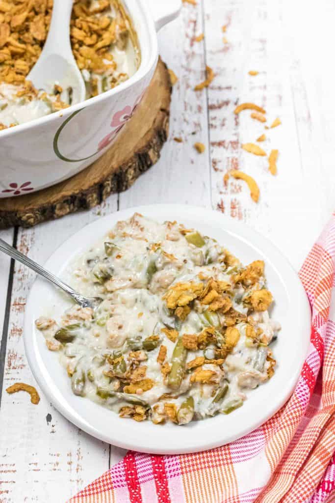 White bowl of green bean casserole with a white casserole dish of it behind it.