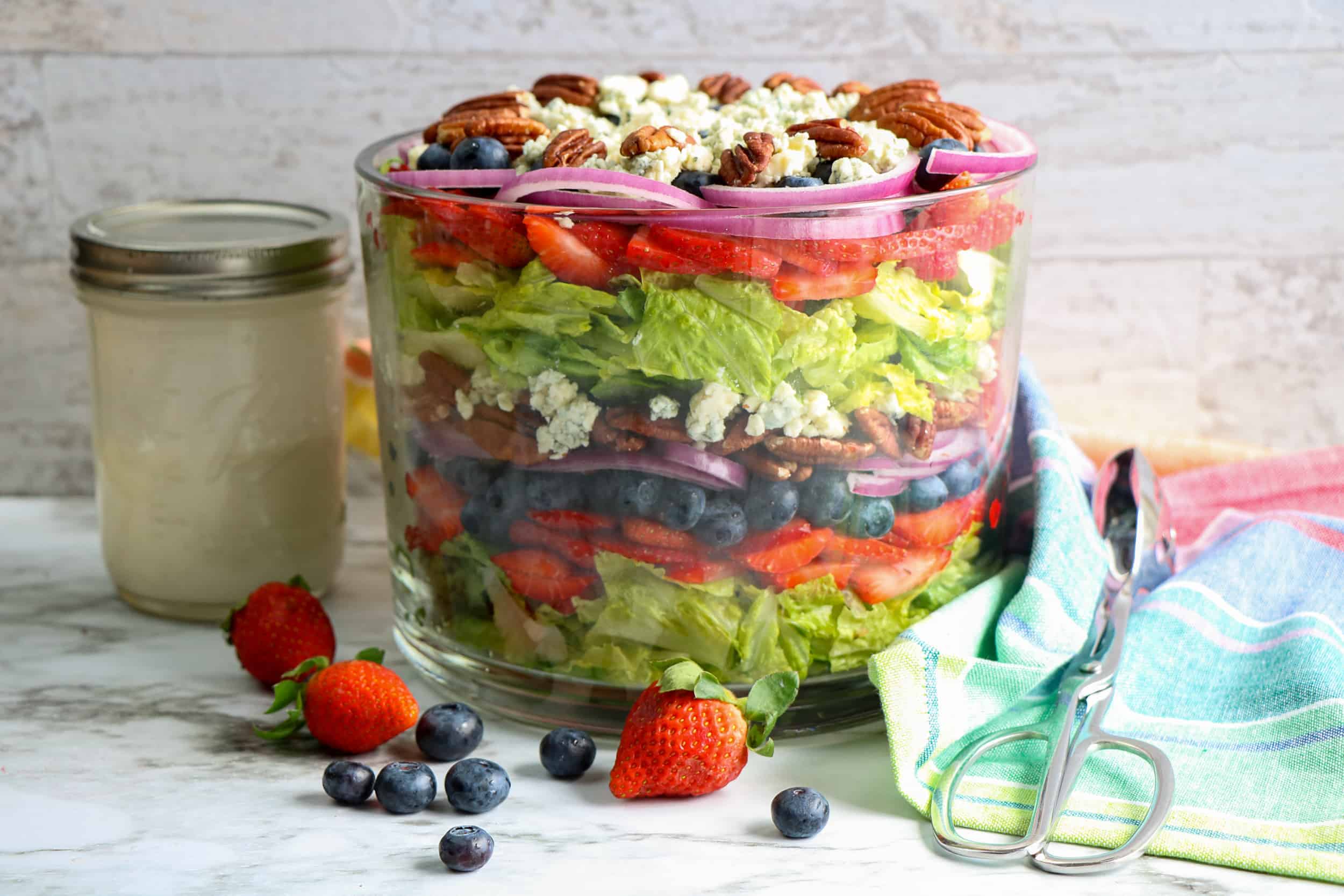 Head-on view of blueberry strawberry salad and buttermilk dressing in a Mason Jar on the side.