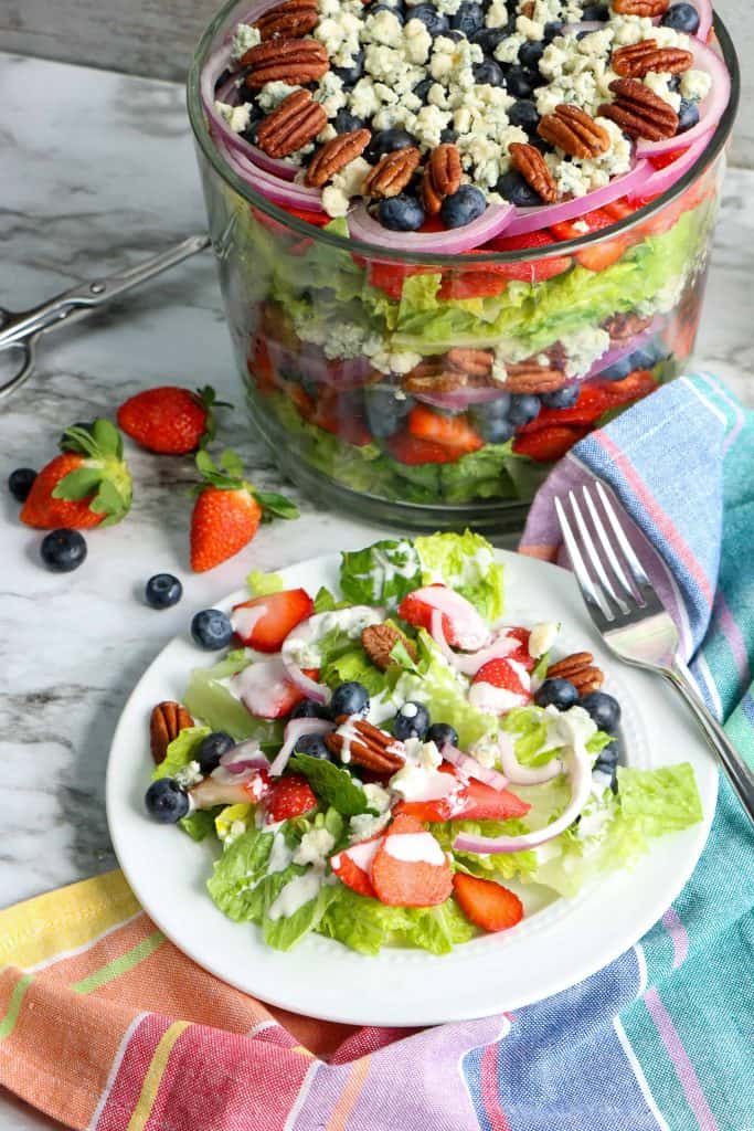 Plate of salad with fruit with trifle bowl filled with salad in the background.