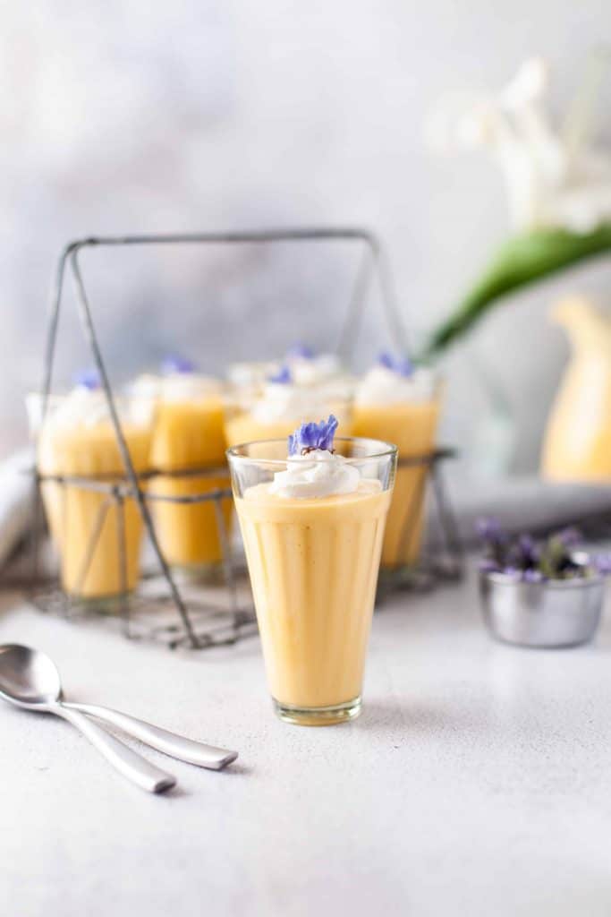 Smoothie with whipped cream and floral garnish with carrying tray of drinks behind it.