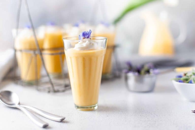 Mango Yogurt Smoothie in a tall glass with purple flower garnish.