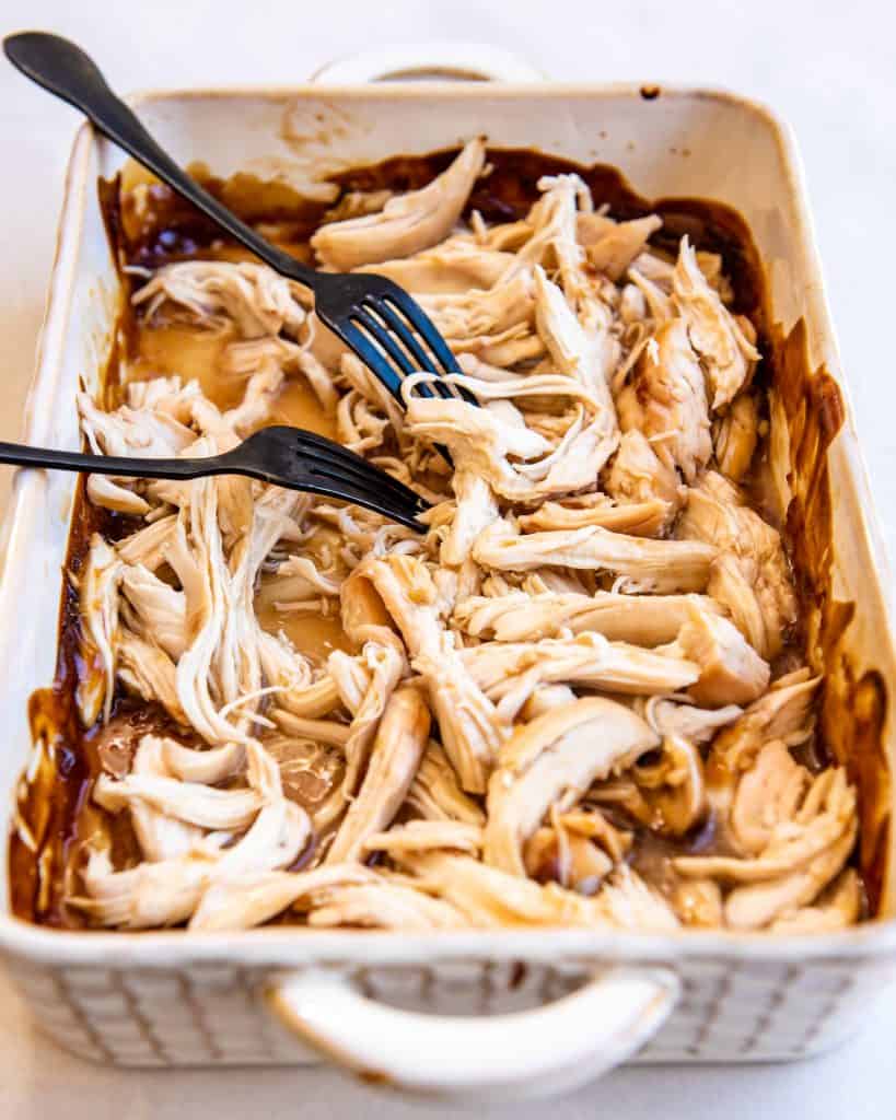 Shredded chicken in a casserole dish with two forks in it.