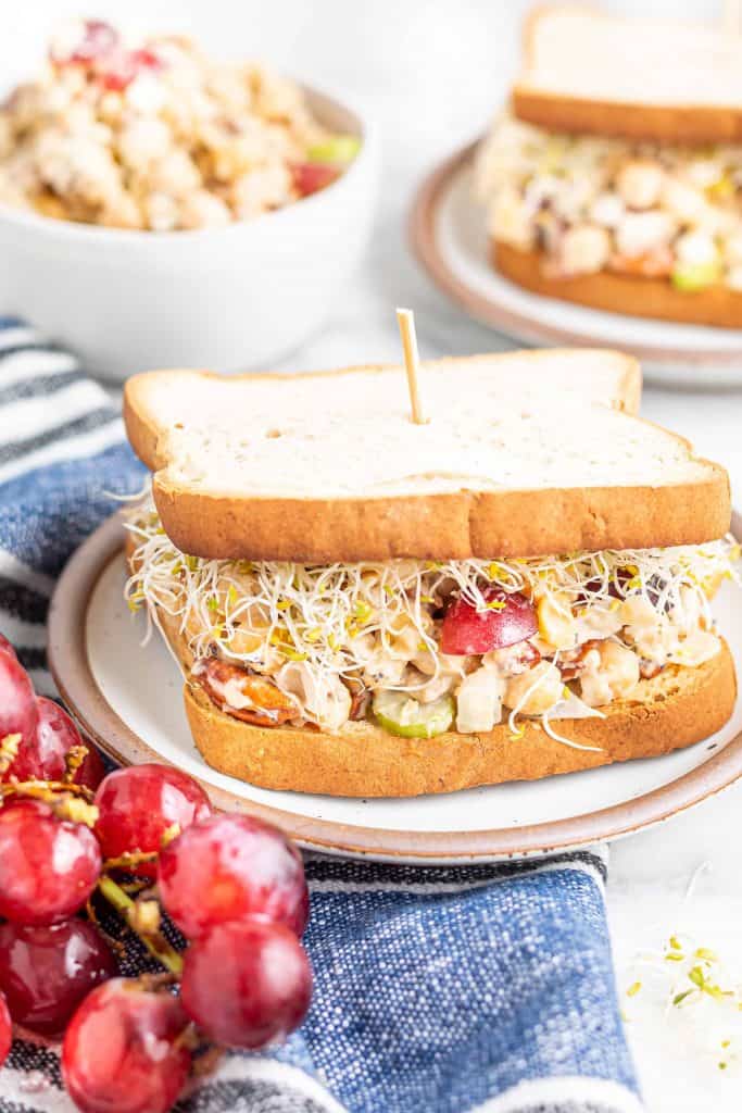 Chickpea Salad Sandwich with grapes and sprouts on white bread with a toothpick in the center holding it together.