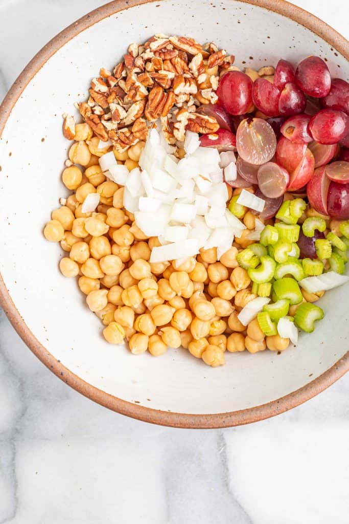 Chickpeas, celery, grapes, onions and pecans in a white ceramic bowl