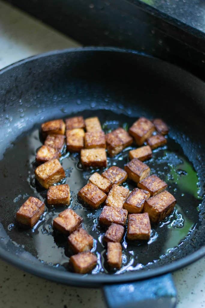 Crispy tofu in a frying pan with oil.