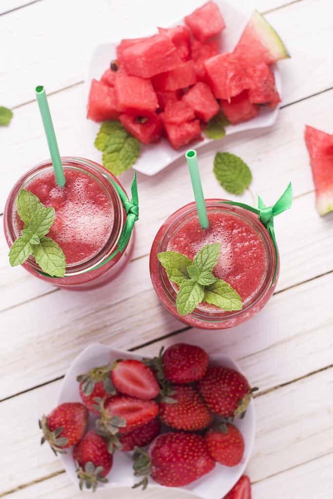 Overhead view of two watermelon strawberry smoothies with watermelon chunks on the side and whole strawberries on the other side.
