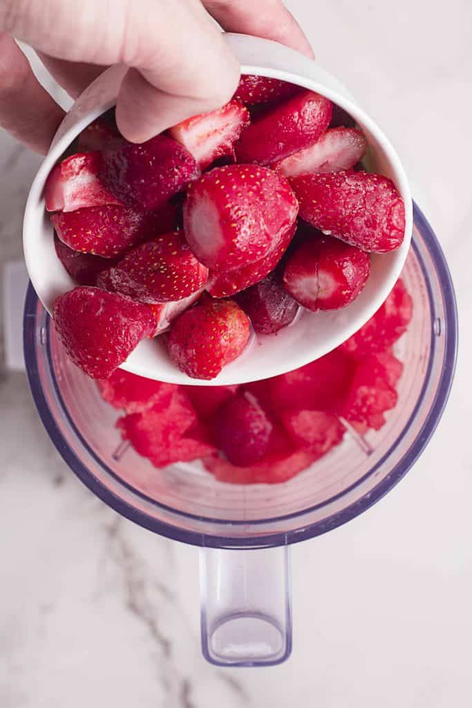 Strawberries being added to a blender with watermelon.