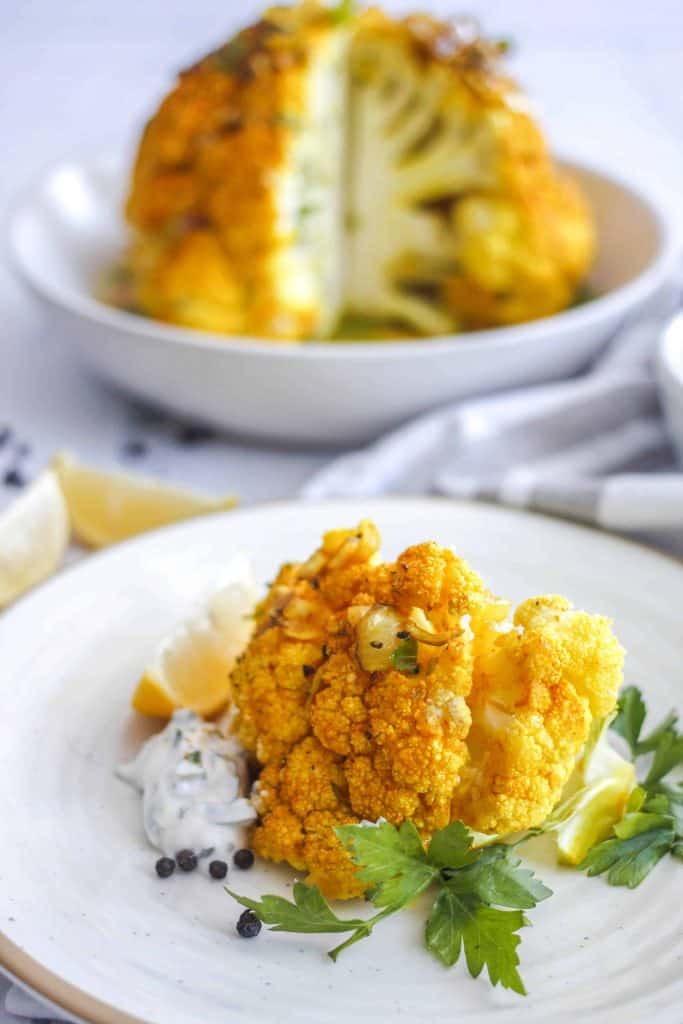 Plate with roasted curried cauliflower and a head of curried cauliflower in the background.