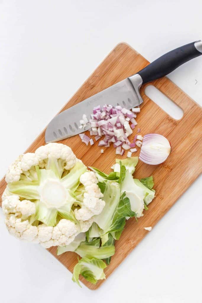 Cauliflower and red onion on a cutting board with a Chef's knife.