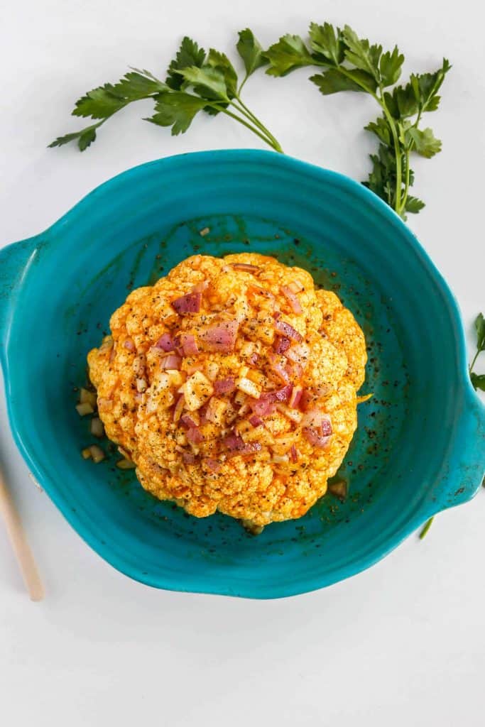 Cauliflower with curry sauce topped with red onions in a blue bowl.