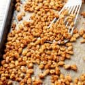 Crispy white beans hot out of the oven on a baking sheet with a spatula scooping some up.