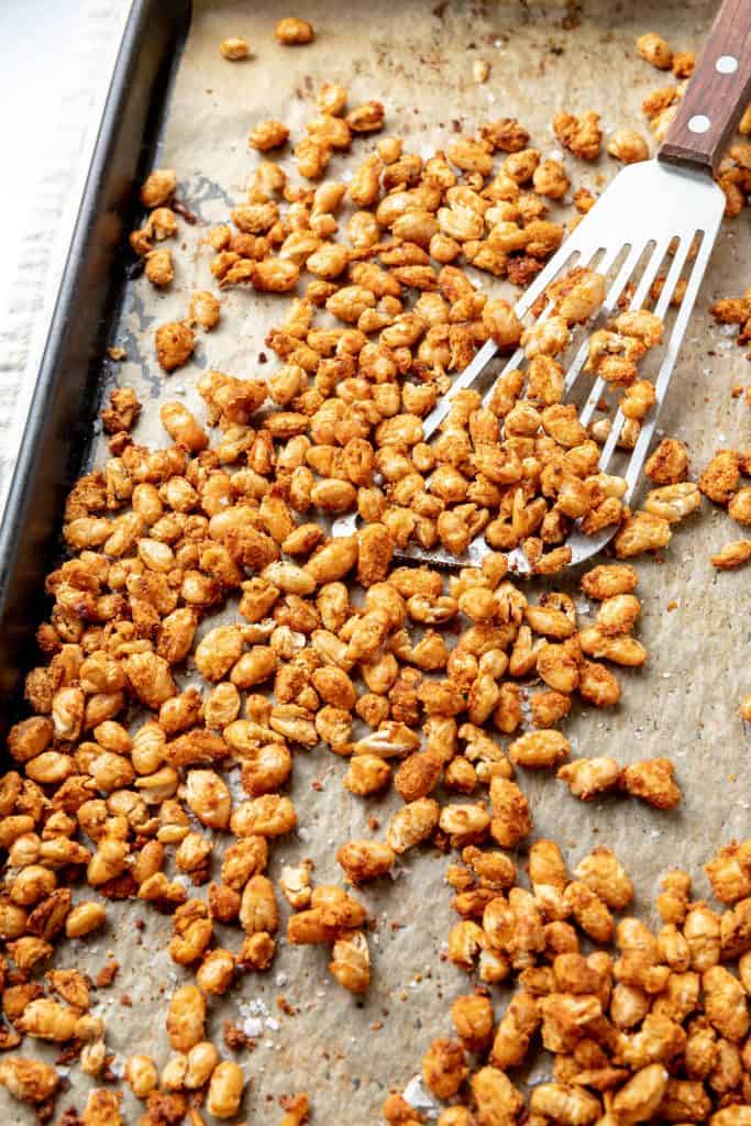 Crispy white beans hot out of the oven on a baking sheet with a spatula scooping some up.