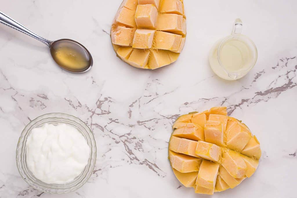 Mango, honey, lemon juice and yogurt on a marble counter top.