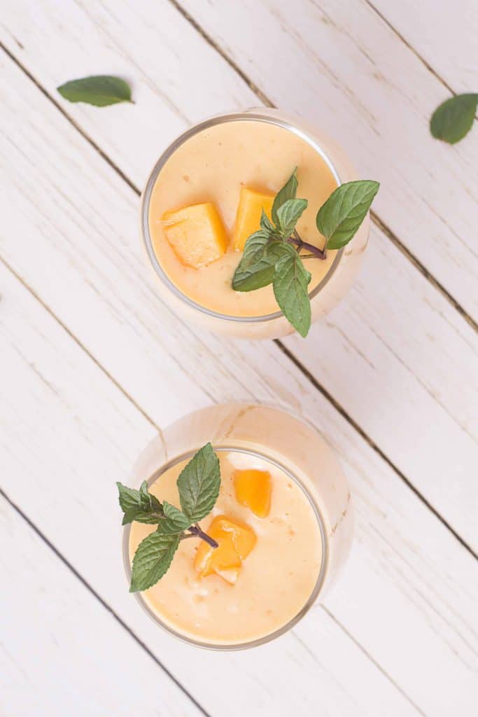 Overhead photo of mango lassis with fresh mint and mango chunks.