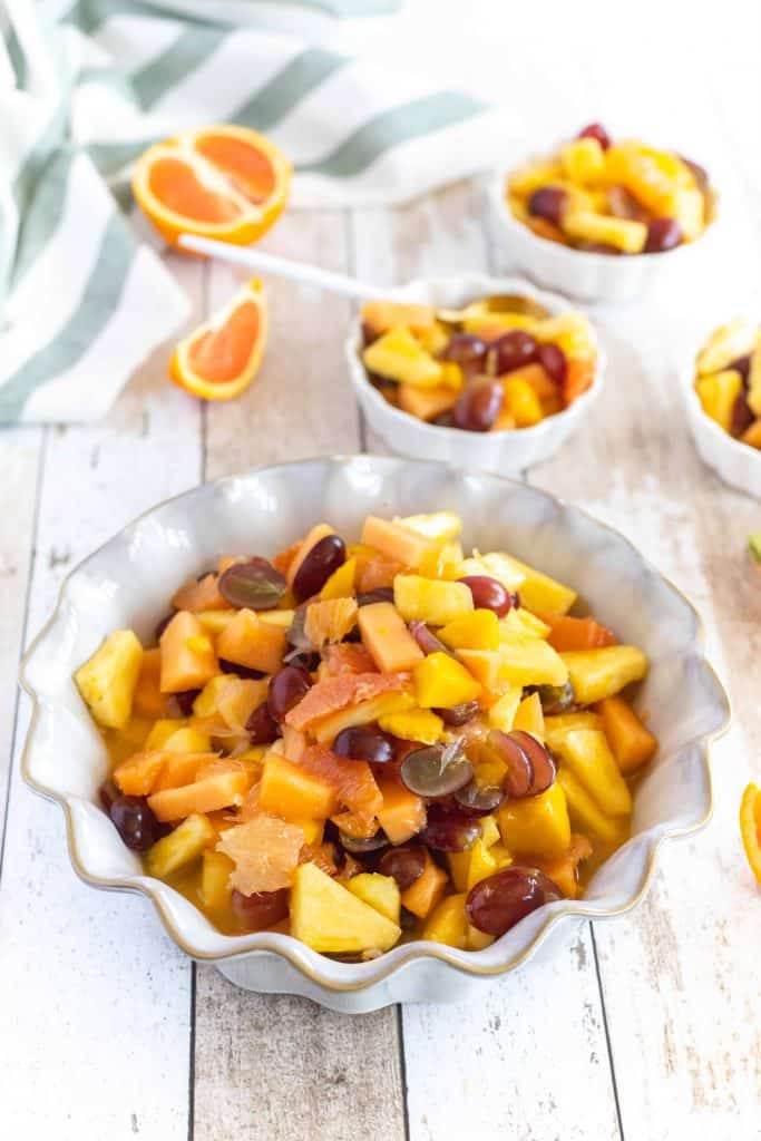 Long lasting fruit salad in a white bowl with small bowls of fruit salad served behind it.