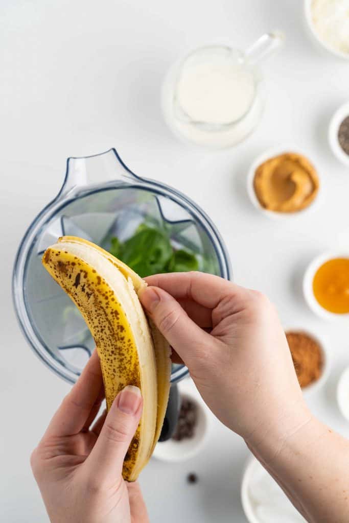 Banana being peeled and placed in blender with spinach.