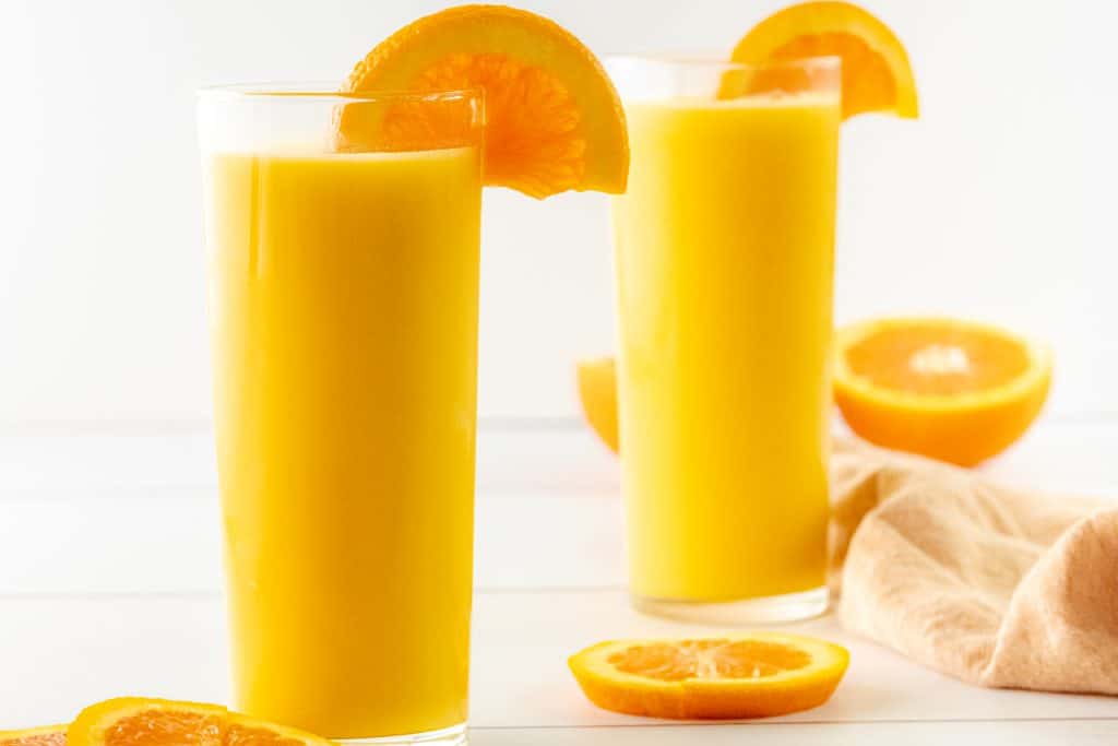 Side by side Orange Julius drinks with orange slices.