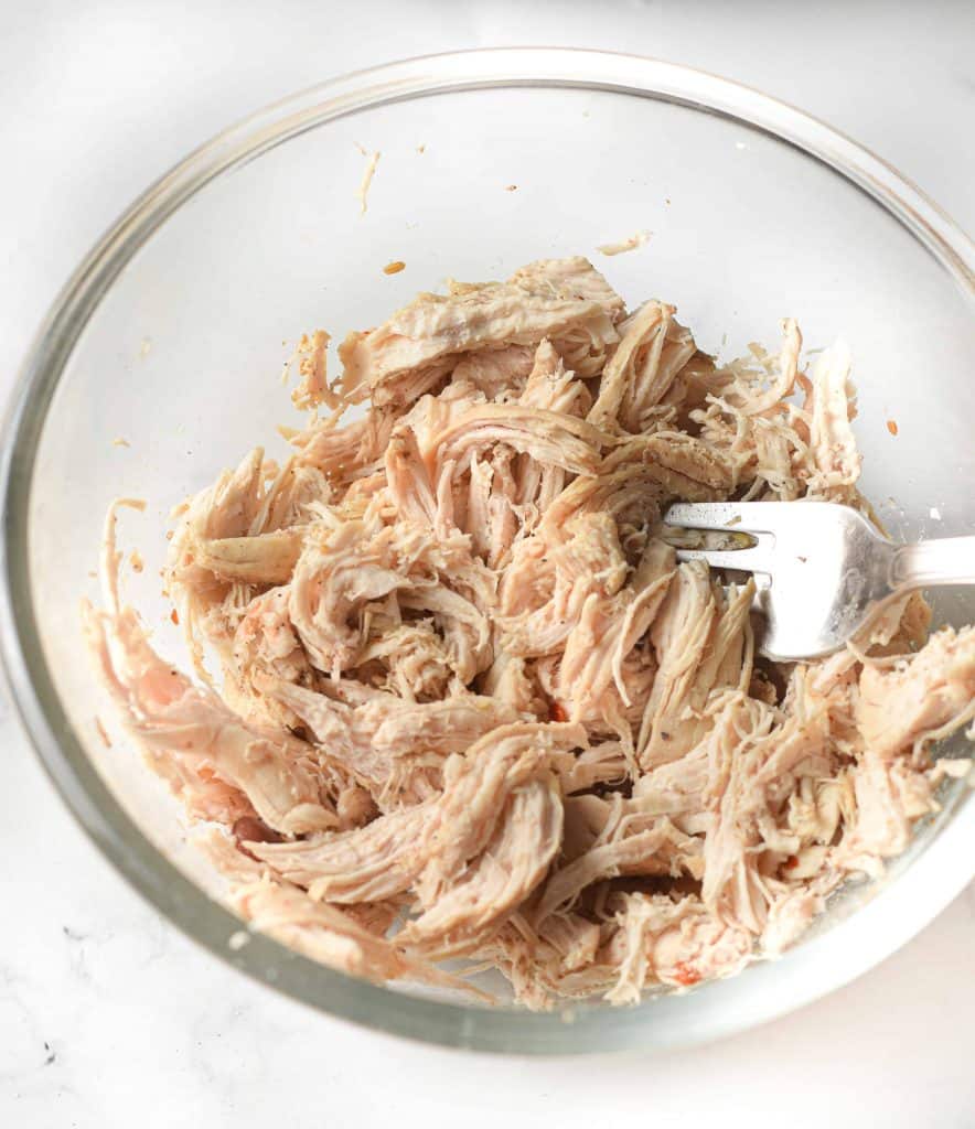 Shredded chicken in a glass bowl with a fork in the chicken.