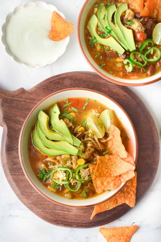 Overhead view of Instant Pot Chicken Tortilla Soup in a white bowl on a wooden cutting board.