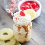 Pineapple milkshake a wood background with pineapple slices and bowl of cherries.