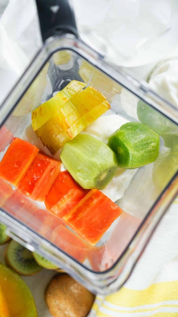 Overhead view of blender with papaya, kiwi, starfruit and ice in it.