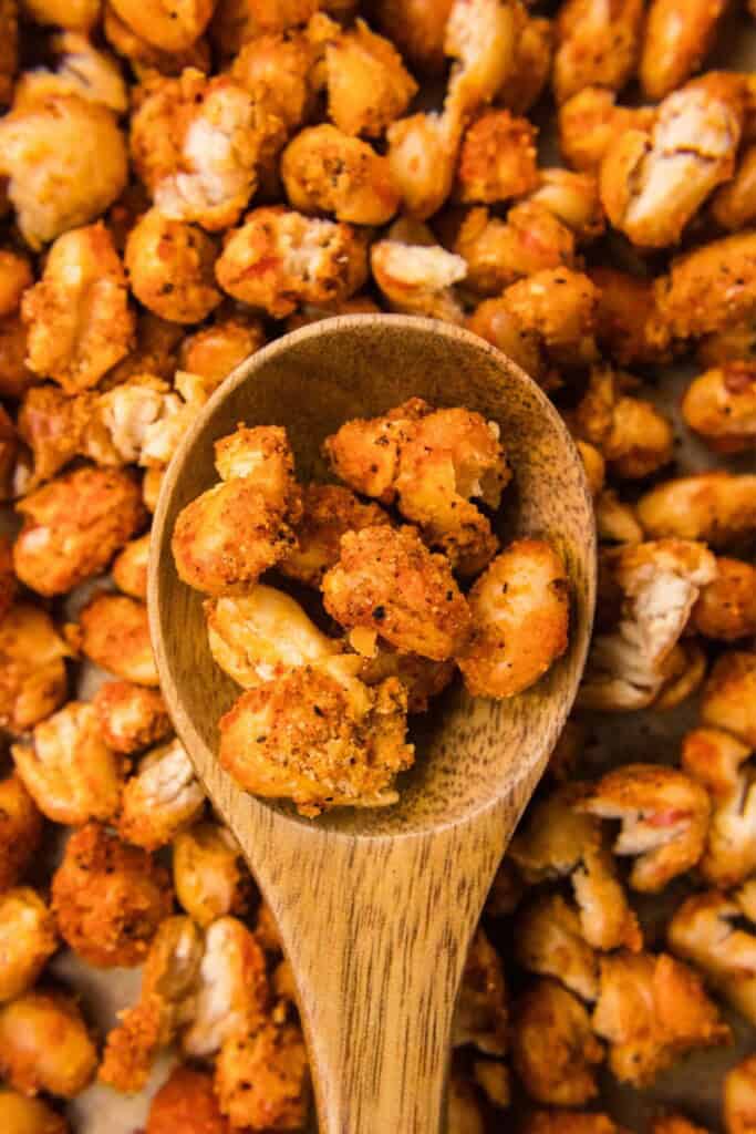 Close-up of crispy roasted white beans on a wooden spoon showing the crackled spice coating and split, puffed texture.