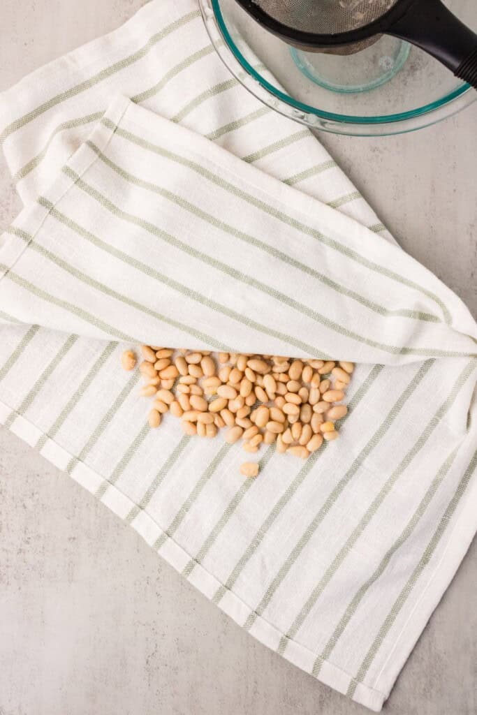 Drained white beans spread on a green and white striped linen towel ready to be dried before roasting.