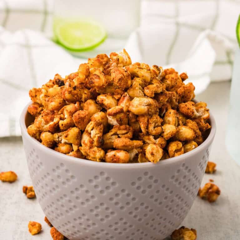 Crispy white beans recipe in a textured gray bowl with lime and seltzer alongside on a light surface.