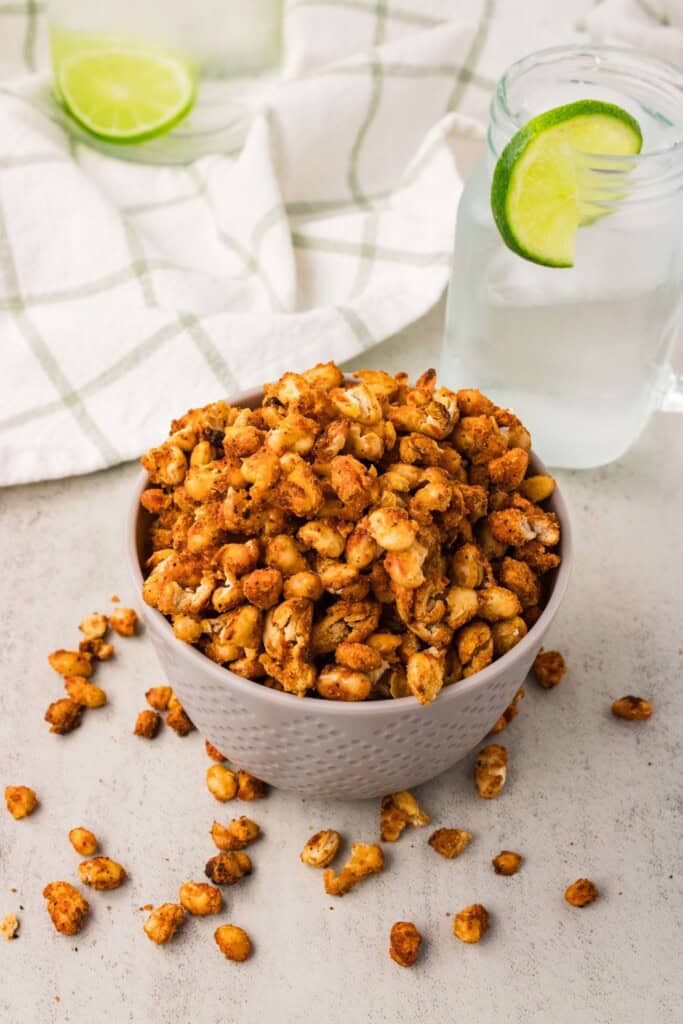 Crispy white beans recipe in a white textured bowl with a lime seltzer alongside on a light surface.