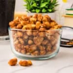 Crispy white beans in a small glass bowl on a marble surface with a cola, plant, and stacked books — a snack alternative to chips.