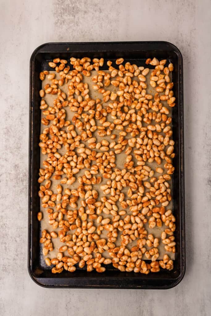 Seasoned white beans spread in a single layer on a parchment-lined sheet pan ready to go into the oven.