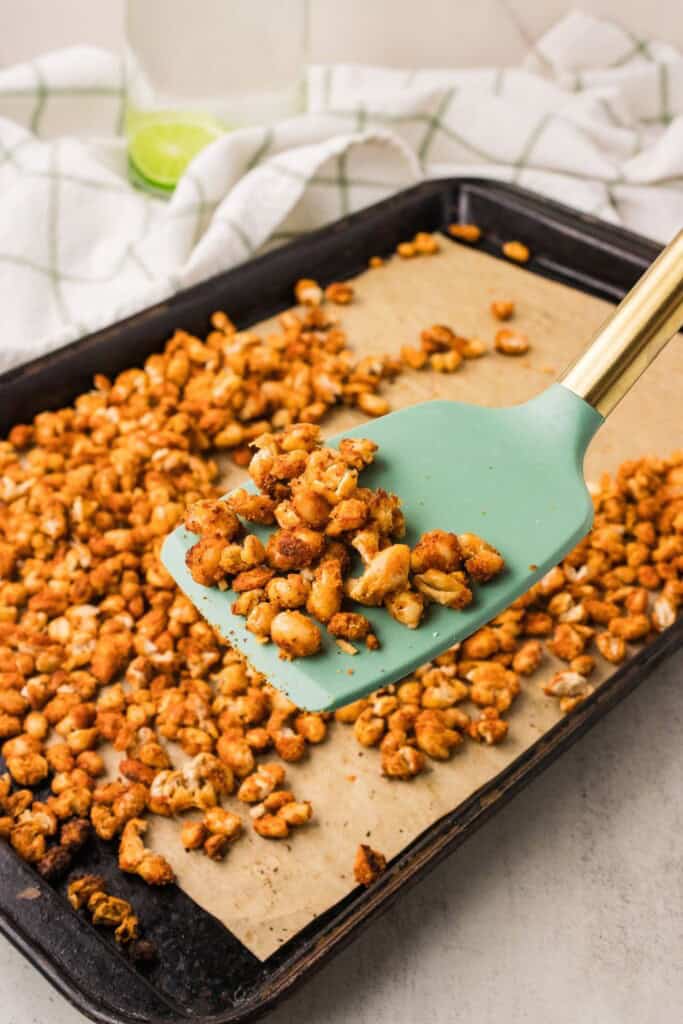Finished crispy roasted white beans on a sheet pan with a teal spatula scooping a portion to serve.