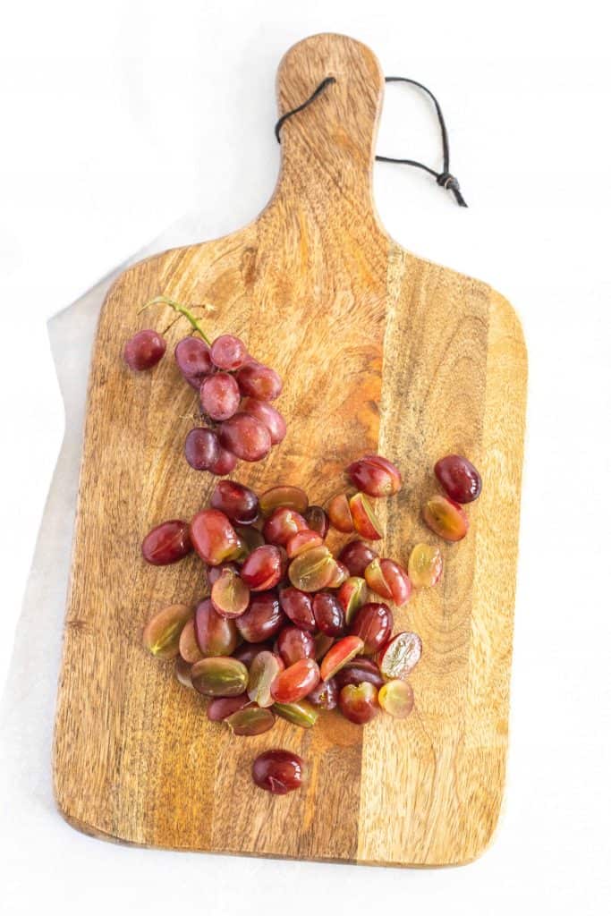 Grapes sliced in half on a cutting board.