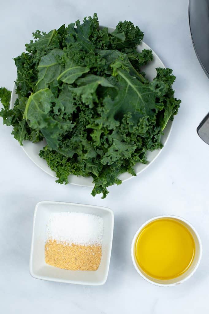 Kale, salt, garlic powder and olive oil on a white counter top.