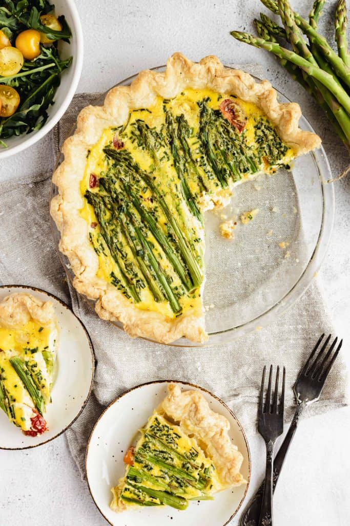 Asparagus and tomato quiche in a pie plate with 2 slices cut out of it.