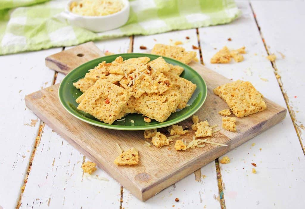 Low Carb Cheese Crackers on a green plate on a cutting board with crackers surrounding it.