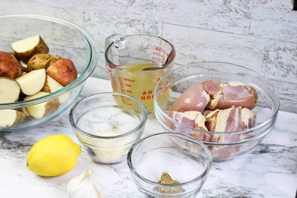 Chicken thighs, chicken brith, lemon, garlic, potatoes on a countertop.