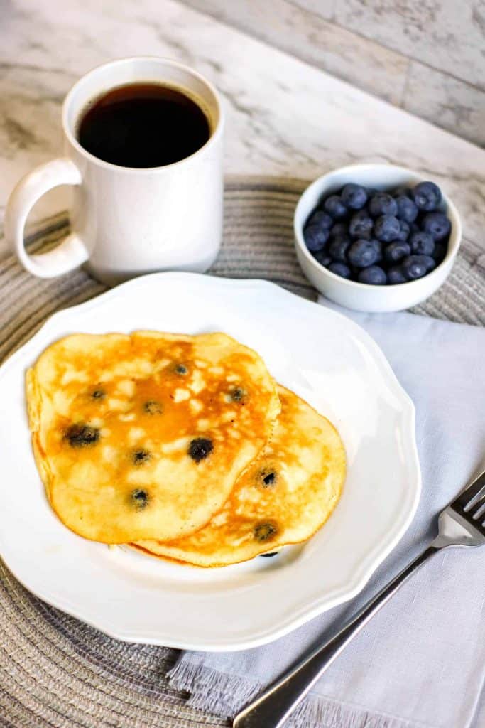 &frac34; angle view of pancakes on a white plate with blueberries and coffee.
