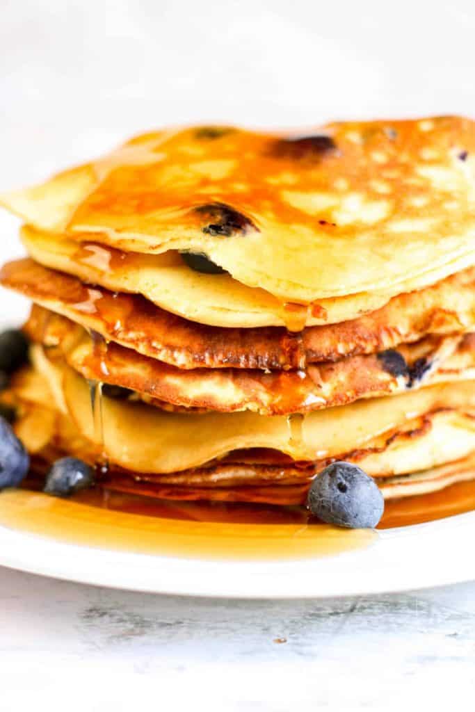 A stack of Keto Blueberry Pancakes with syrup dripping over the side.