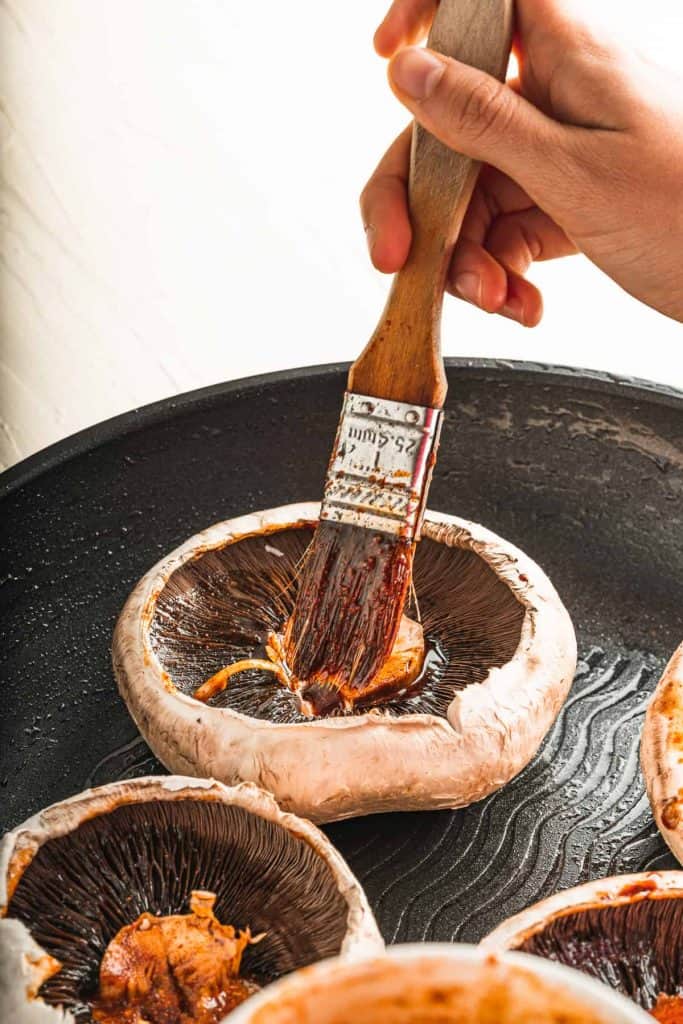Brushing marinade on portobello mushrooms.
